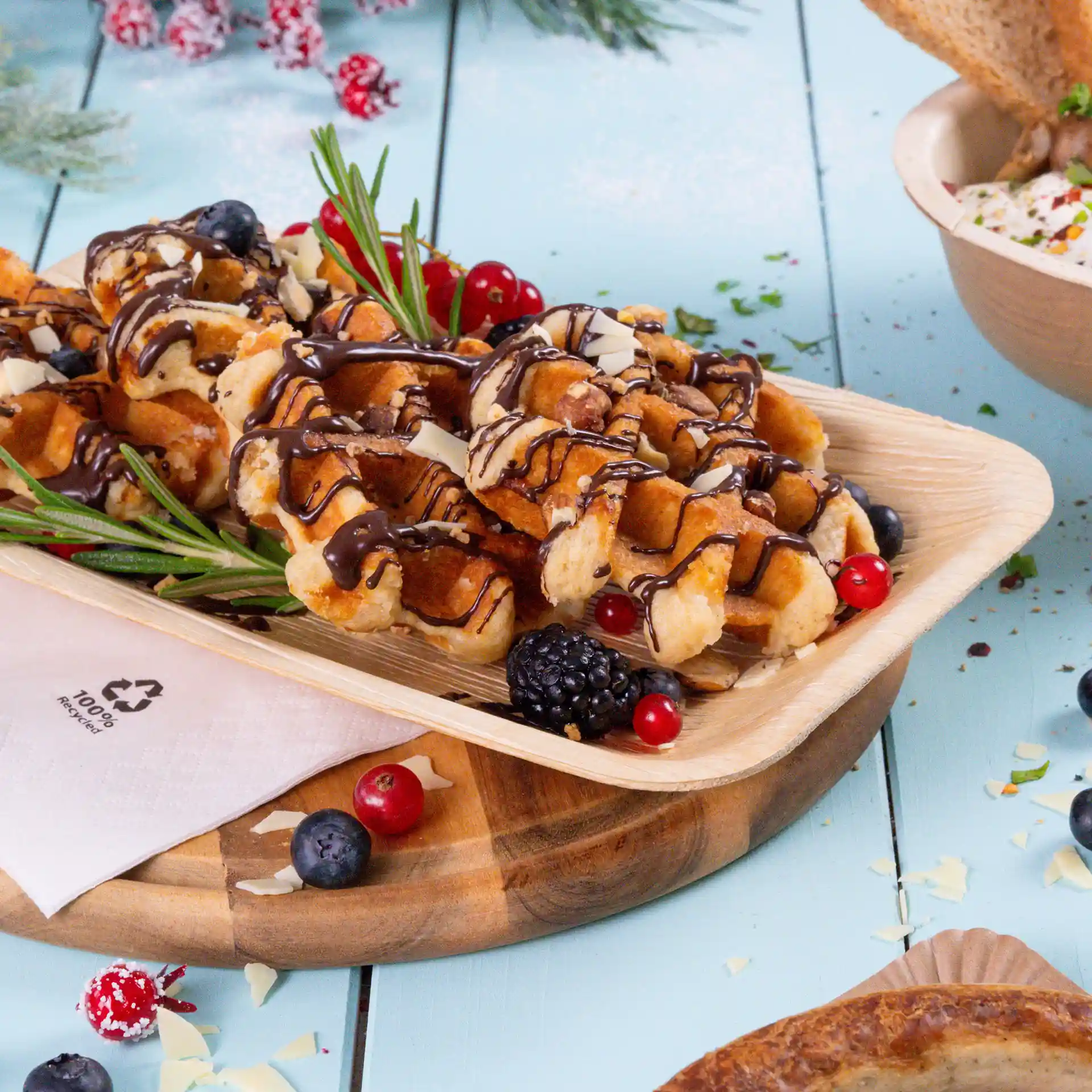 Waffle guarnite con salsa di cioccolato, scaglie di cioccolato bianco e bacche su un piatto di foglia di palma.