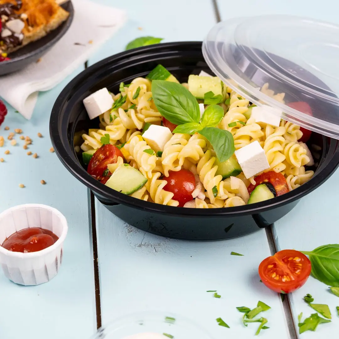 Ciotola nera con insalata di pasta contenente rotini, pomodorini, cetriolo, feta e basilico, con un lato di ketchup.