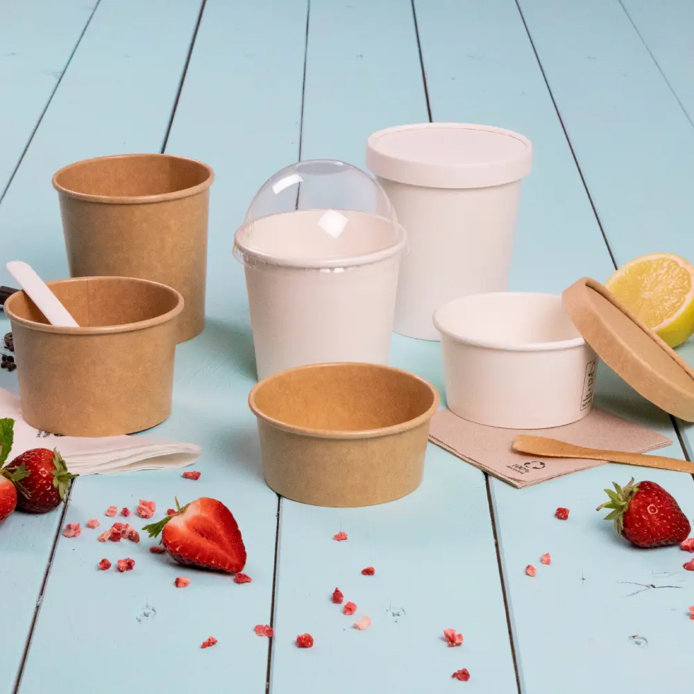 Contenitori per dessert da asporto di varie dimensioni, in carta e plastica, circondati da fragole e limone.