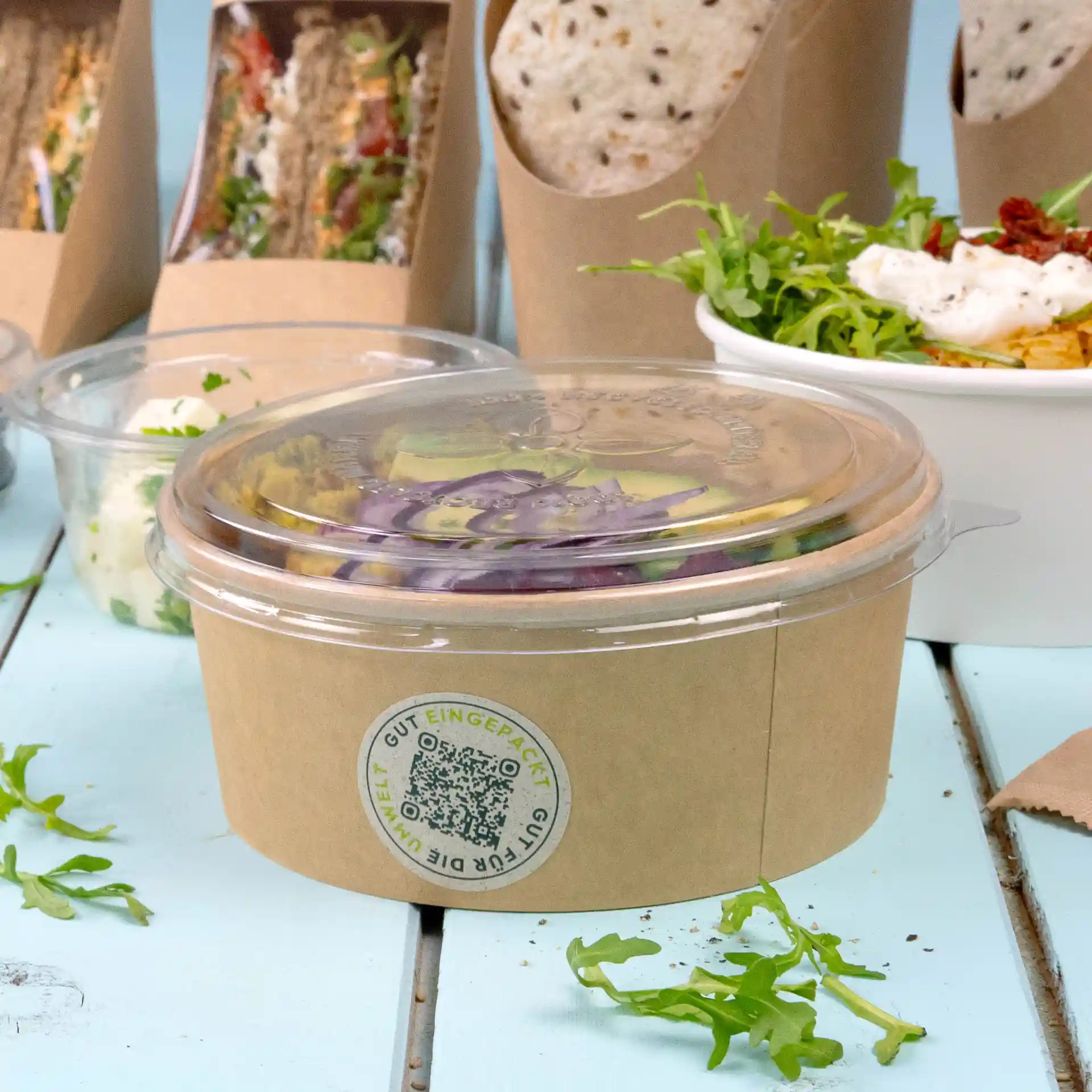 Bicchiere rotondo trasparente con coperchio trasparente, contenente insalata e un'etichetta con design circolare.