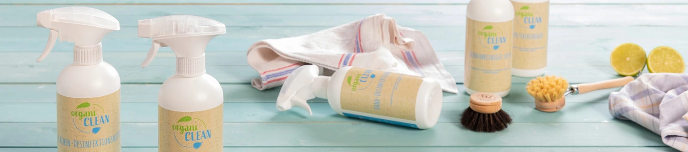 Due bottiglie spray di soluzione detergente con etichette, un panno, una spazzola e lime a metà su una superficie in legno blu.