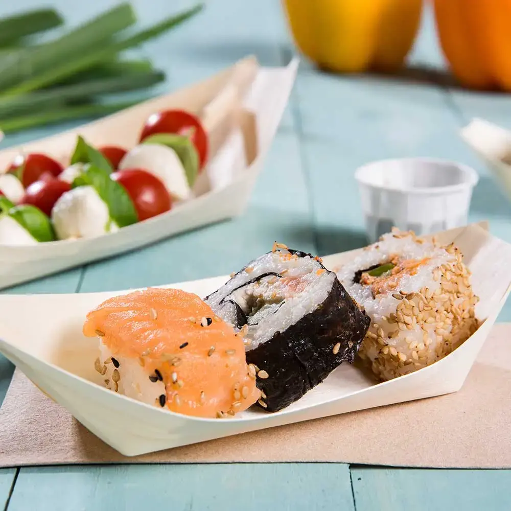 Rolls di sushi serviti in un piatto a forma di barca di legno, con salmone, sesamo e nori, accompagnati da pomodorini e mozzarella.