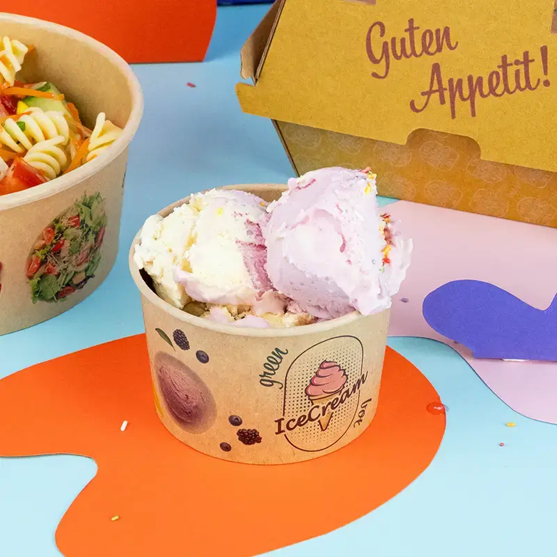Becher verde pieno di più palline di gelato, guarnito con frutta e noccioline, su sfondo azzurro.