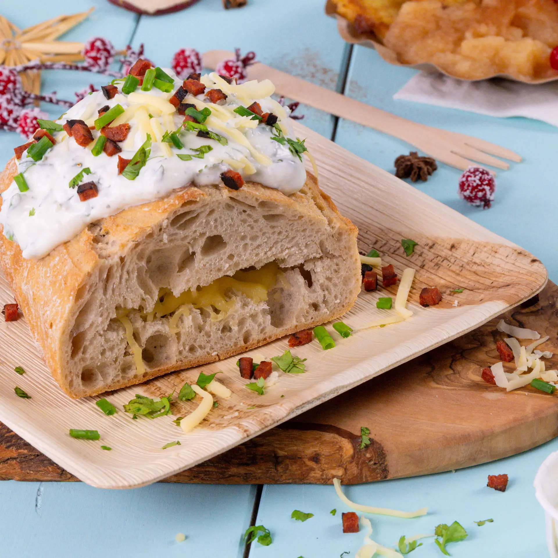 Piatto quadrato in foglia di palma con una pagnotta affettata guarnita con salsa, formaggio ed erbe, mostra un motivo di grano naturale.