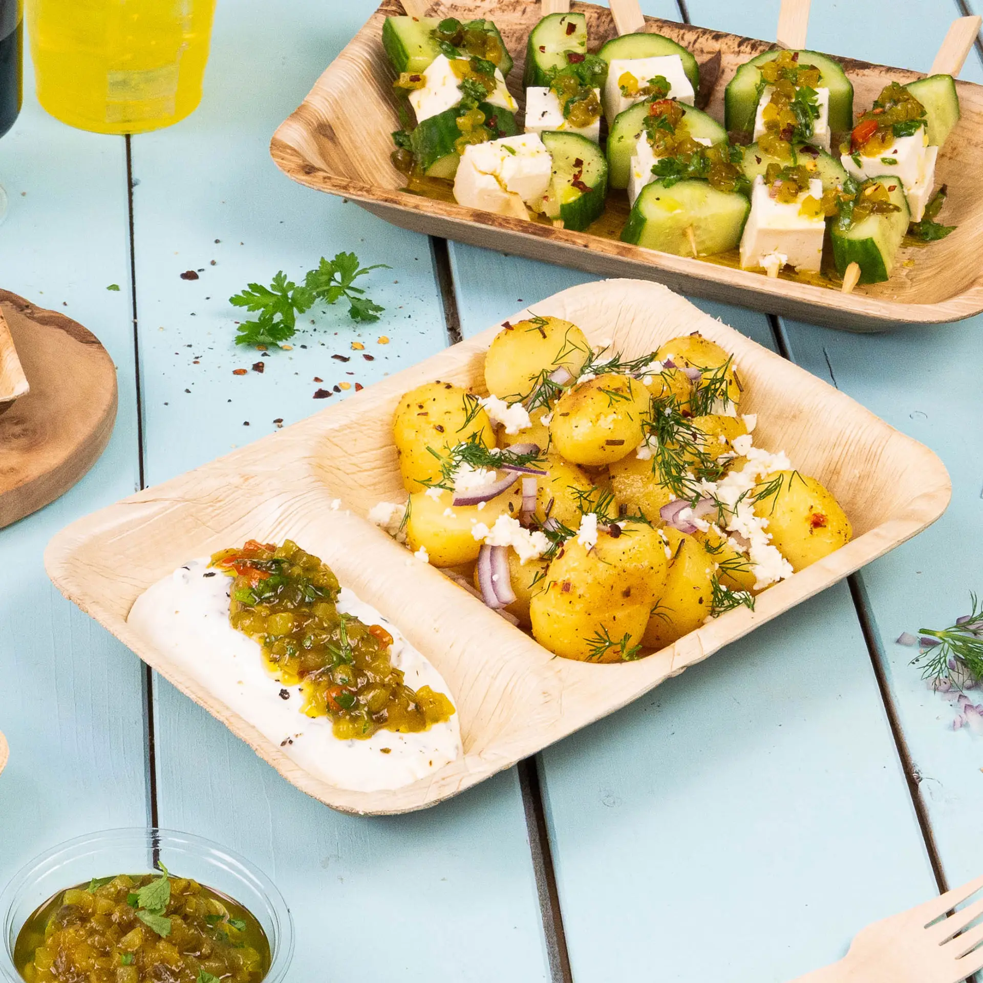 Piatto da menu a tre scomparti in foglia di palma con hummus, verdure saltate e ravioli su sfondo blu chiaro.