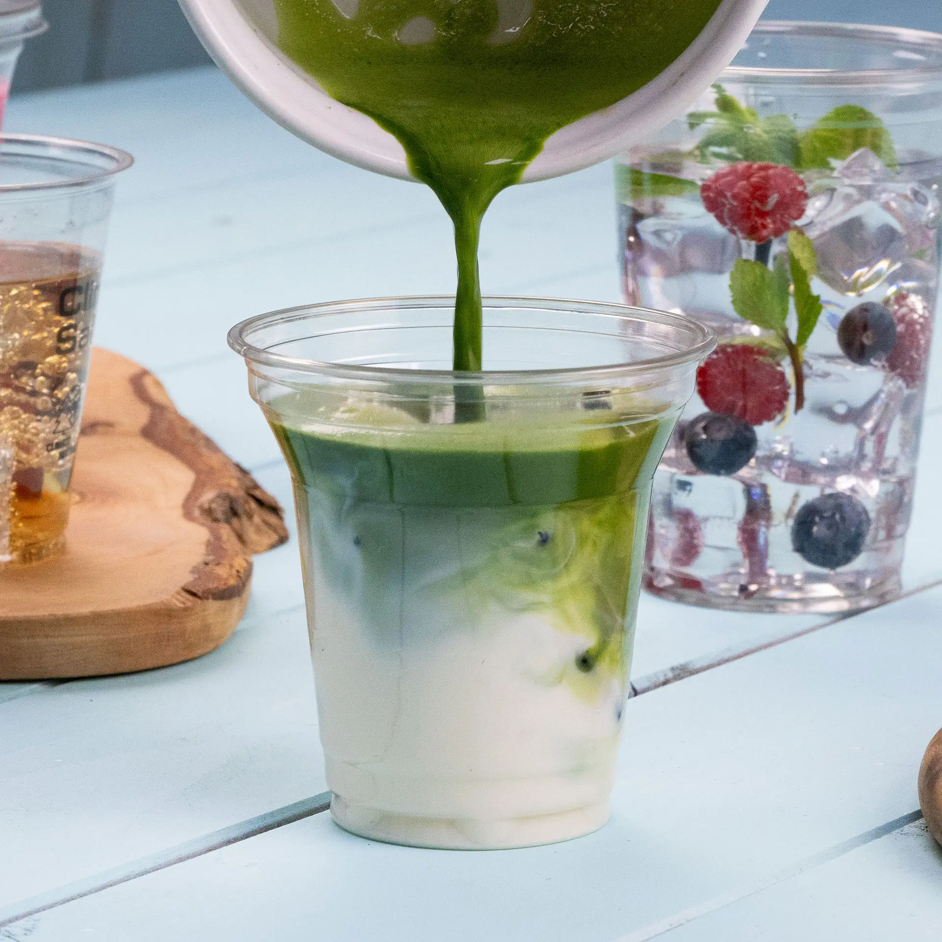 Un bicchiere in rPET trasparente viene riempito con una bevanda verde, mostrando strati di colore; altre bevande sono visibili sullo sfondo.