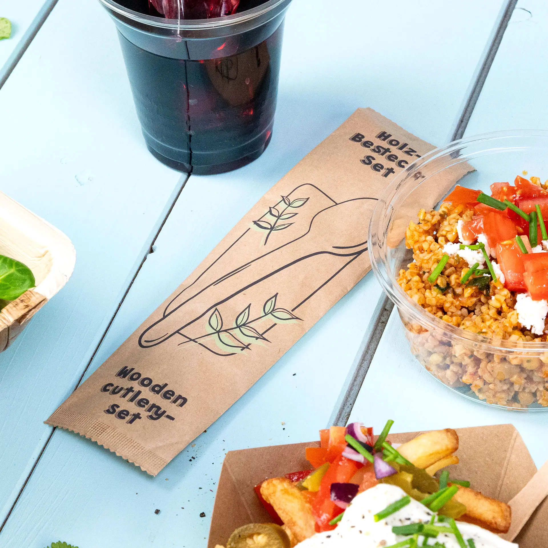 Set di posate in legno con cucchiaio e tovagliolo esposto; include una busta biodegradabile e adatto per cibi caldi o freddi.