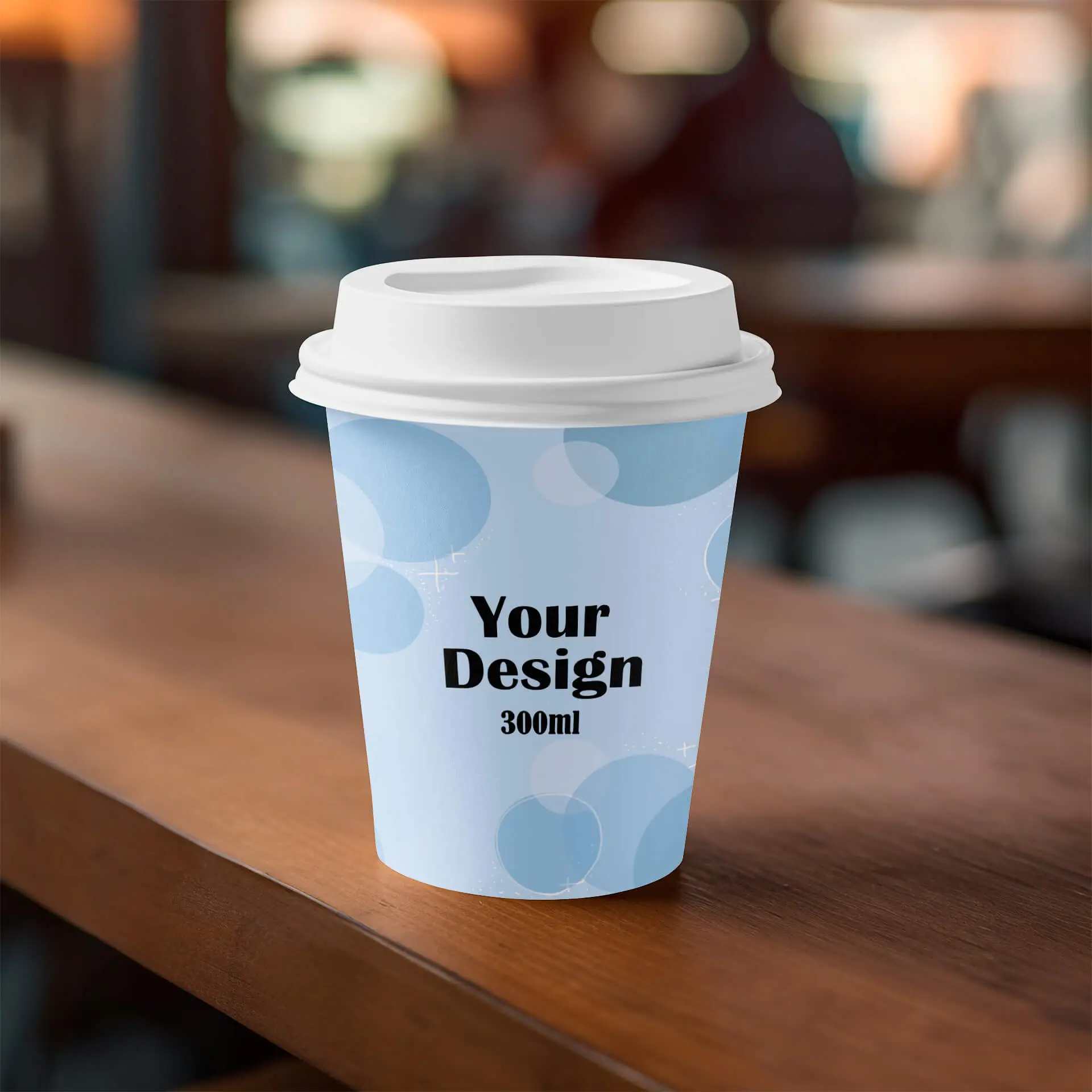 Bicchiere di carta con un coperchio bianco, con un design azzurro e testo nero, posato su una superficie di legno.