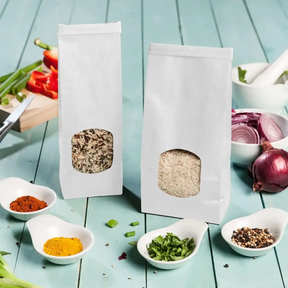 Due sacchetti di carta bianchi contenenti riso e un mix di cereali, circondati da piccole ciotole di spezie e verdure tritate.