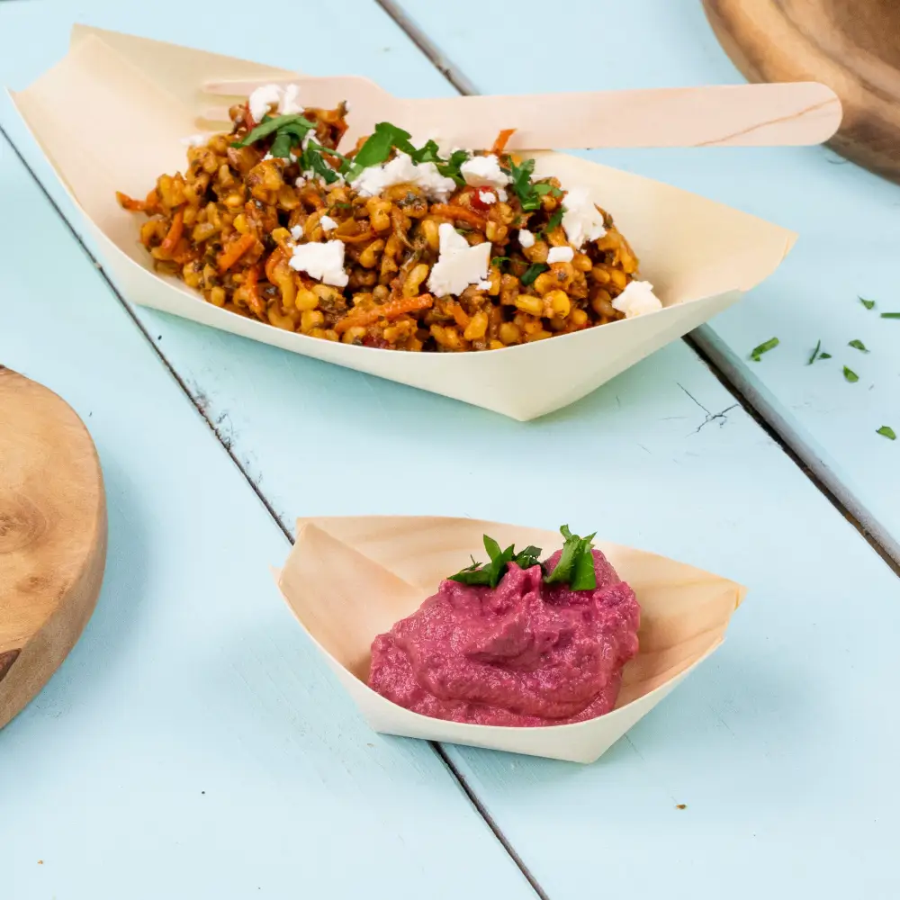 Vassoi in bambù con piatto di verdure miste e salsa rosa, guarniti con erbe, su una superficie in legno azzurro chiaro.