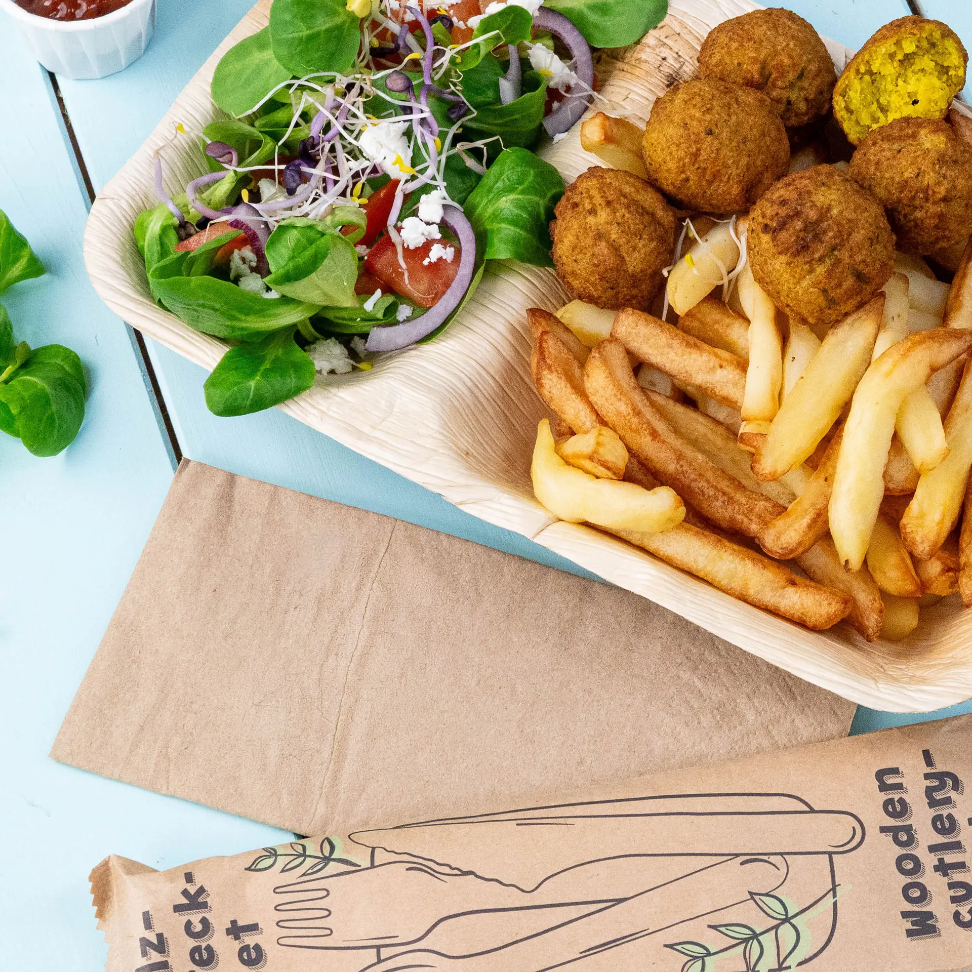 Immagine di un vassoio di legno con polpette di falafel, patatine fritte e un'insalata mista con verdure, pomodori e cipolle.