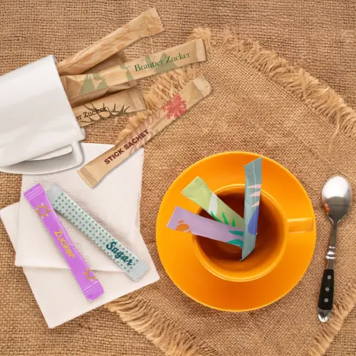 Bustine di zucchero colorate in una tazza di tè su un tavolo rustico con un cucchiaio e tazze vuote.