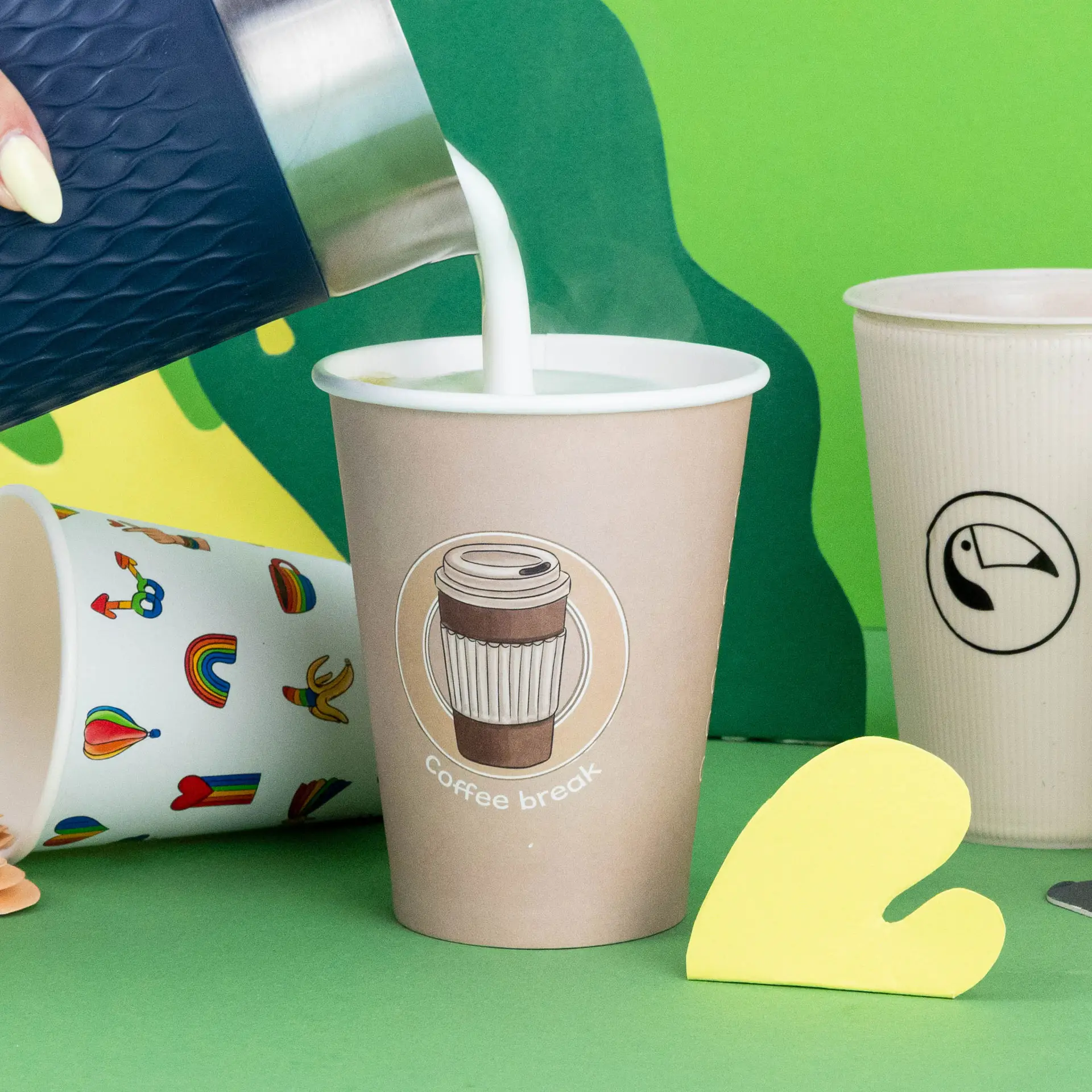 Immagine di un bicchiere di carta con un logo "pausa caffè", riempito di latte, circondato da bicchieri colorati su uno sfondo verde.