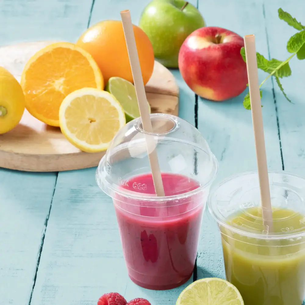 Due bicchieri trasparenti con frullati di frutta, uno rosa e uno verde, posizionati accanto a frutta fresca su una superficie blu.