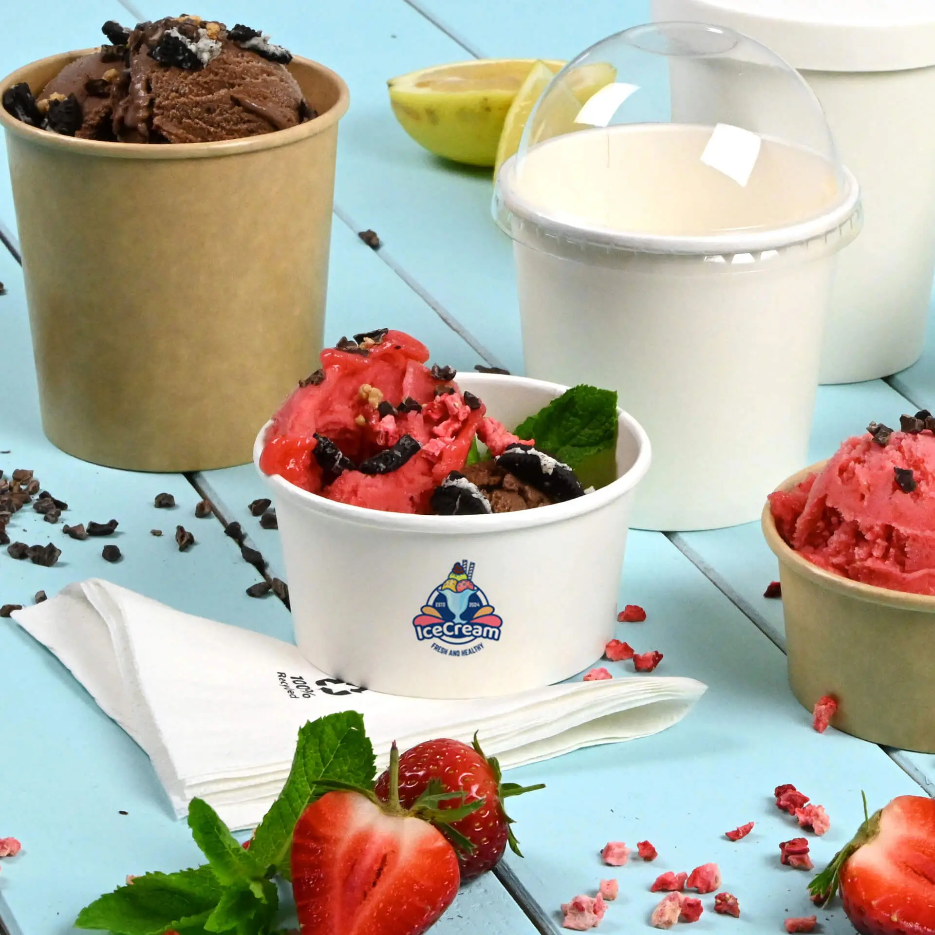 Cup di gelato bianco personalizzato con gelato al cioccolato e fragola; tazze aggiuntive sullo sfondo; fragole e foglie di menta vicine.