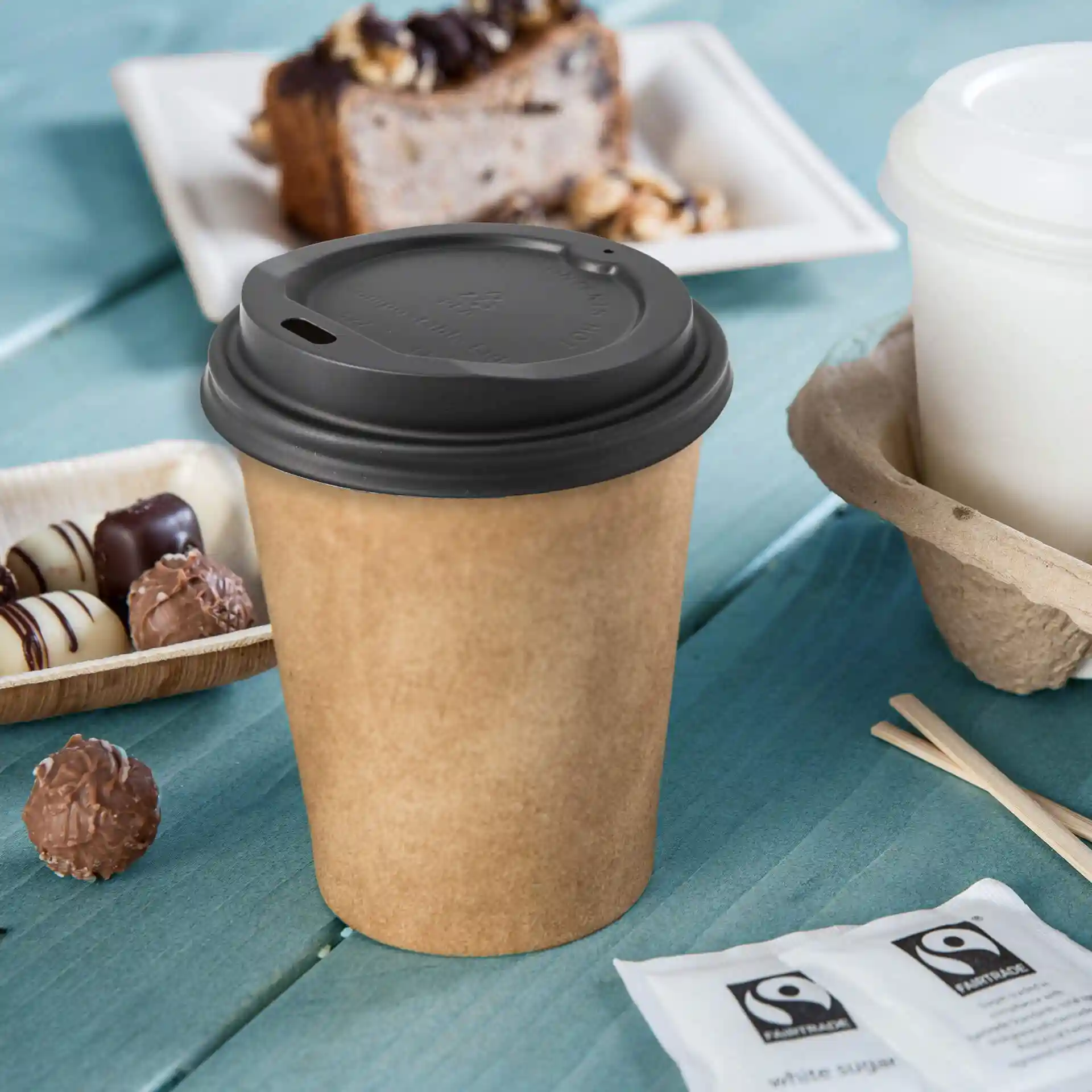 Coperchio per tazza in CPLA nero con foro per bere, posato su una superficie in legno blu con snack nelle vicinanze.