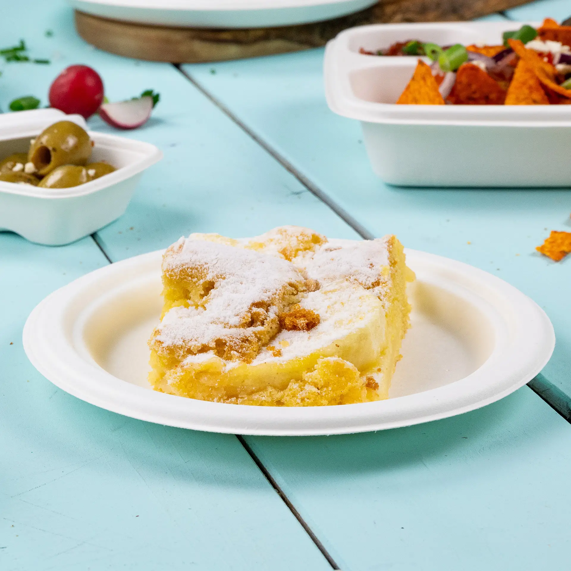 Una fetta di torta cosparsa di zucchero a velo su un piatto rotondo in canna da zucchero biodegradabile su uno sfondo blu.