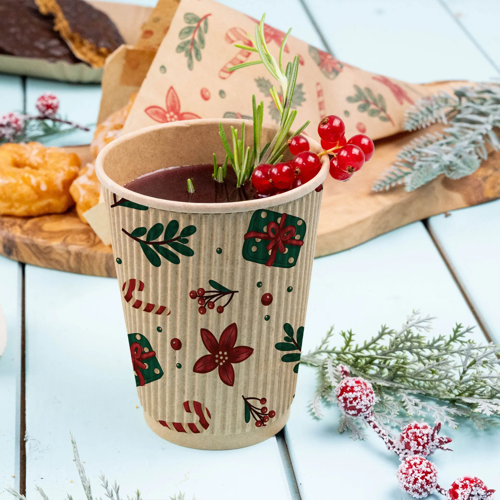 Bicchiere marrone a righe con design invernale, riempito con una bevanda e guarnito con bacche rosse e rosmarino, su una superficie azzurro chiaro.