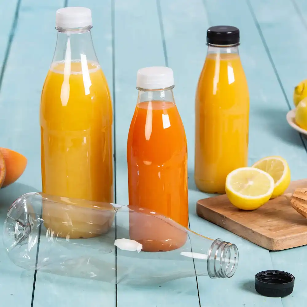 Tre bottiglie di plastica piene di succhi gialli e arancioni, una bottiglia è sdraiata, e un limone e biscotti sono vicini.