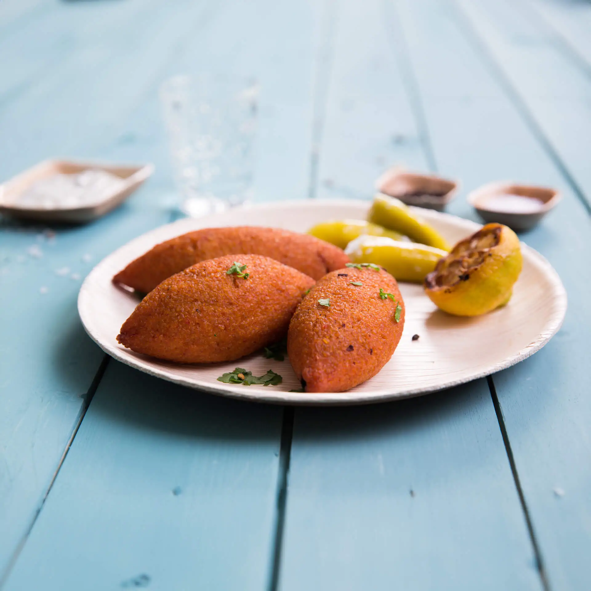 Tre piatti ovali in foglie di palma con bordo sottile, contenenti cibi arancioni, accompagnati da peperoni verdi e una fetta di limone grigliato.