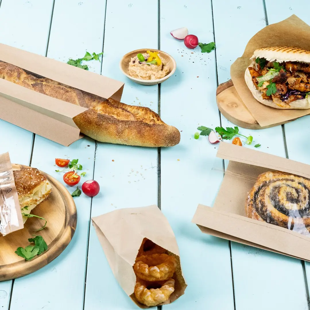 Immagine di vari prodotti da forno tra cui una baguette, un panino, pasticcini e una ciotola di salsa su una superficie in legno blu.