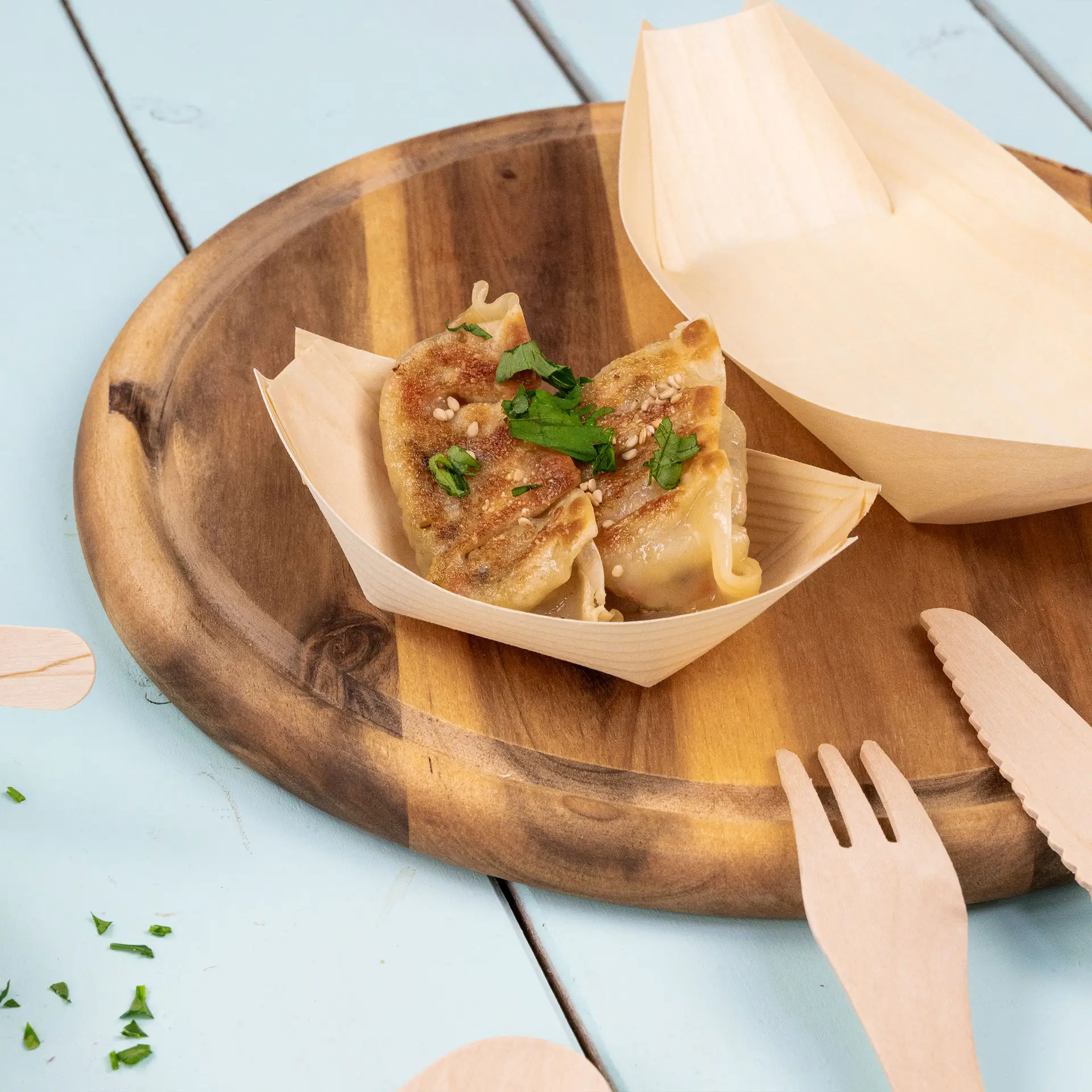 Contenitore a forma di barca in legno con due ravioli guarniti con semi di sesamo e prezzemolo su un vassoio di legno.