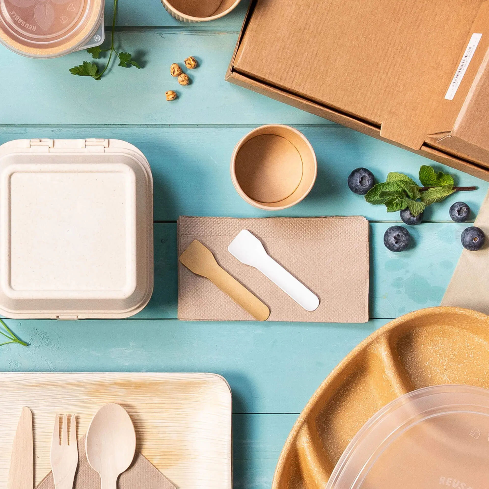 Immagine di vari contenitori alimentari usa e getta, posate e una scatola di cartone su una superficie blu.