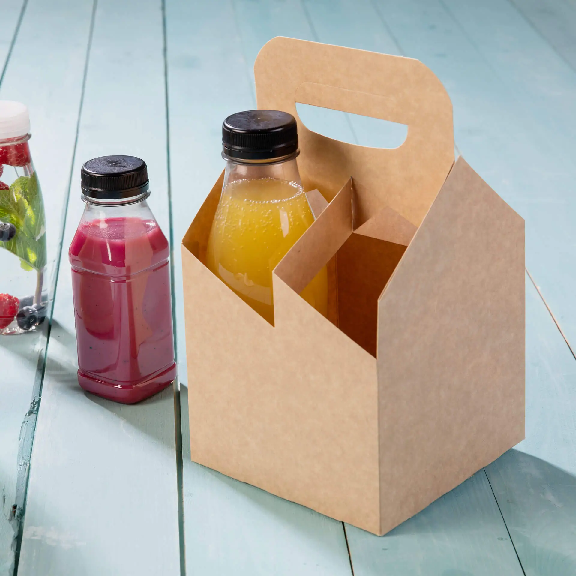 Un portabottiglie in cartone pieghevole con manico centrale, che tiene due bevande; una gialla e una rosa, su una superficie di legno.