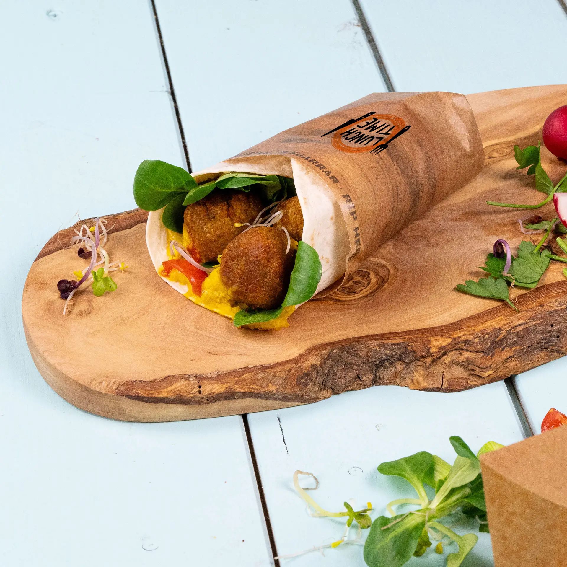 Una borsa avvolgente stampata su misura contenente falafel, verdure e salsa, posta su un vassoio di legno.