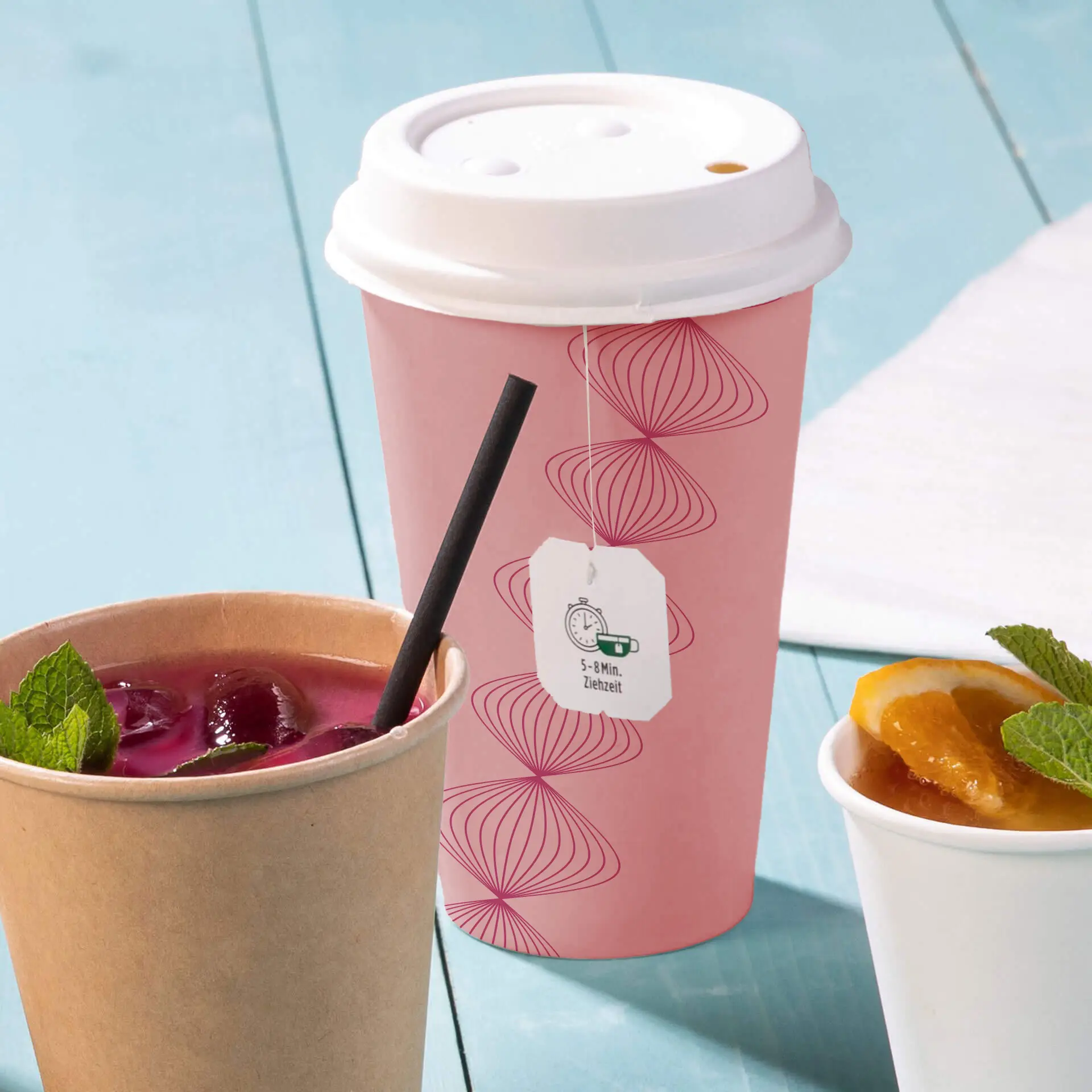 Un cup in carta rosa con design del logo e un coperchio bianco, e due tazze aggiuntive: una beige con una cannuccia e una bevanda scura, e una bianca con cibo e menta.