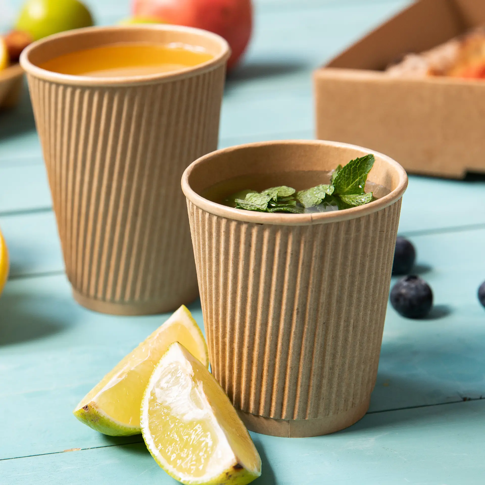 Due bicchieri usa e getta marroni, rigati e isolati per bevande calde, uno con foglie di menta e spicchi di lime accanto.