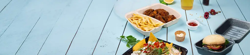 Personaggio chef con testa verde e cappello bianco, in mano un cucchiaio; due contenitori di cibo con un hamburger e un pasto con patatine e pollo su uno sfondo di legno azzurro.