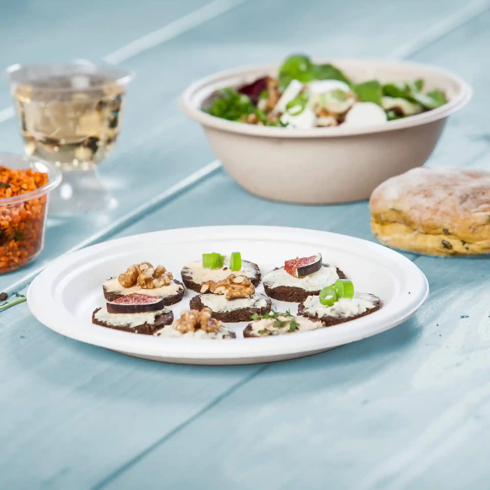Piatto con diverse fette rotonde di pane scuro guarnite con crema, noci e fichi, accanto a un'insalata e un biscotto.