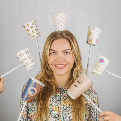 Donna con capelli lunghi che sorride e tiene diversi bicchieri di carta colorati su bastoncini intorno alla testa.