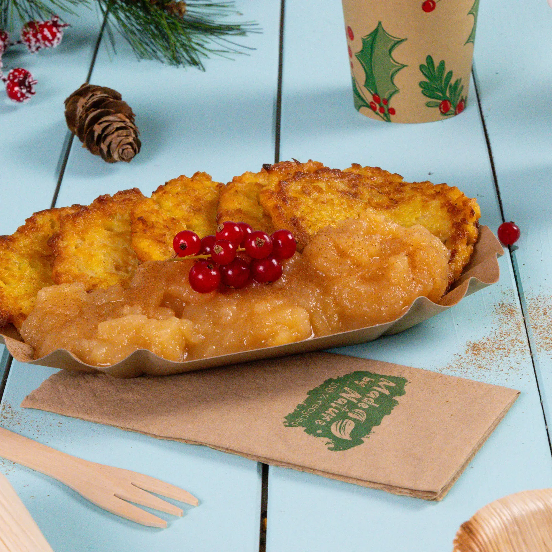 Un piatto di pancake di patate croccanti servito con salsa di mele e guarnito con ribes rossi, accanto a un tovagliolo di carta e elementi decorativi.