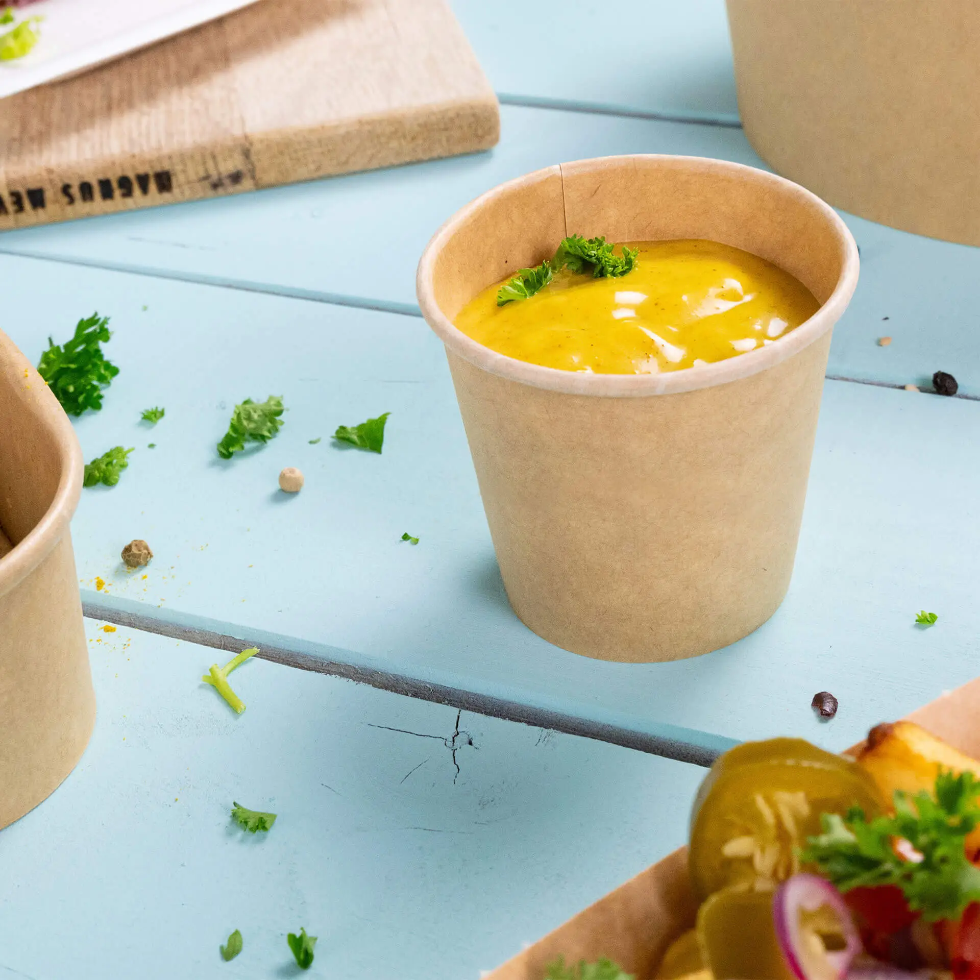 Una coppetta di carta non sbiancata riempita di salsa gialla e guarnita con prezzemolo, su una superficie di legno blu.