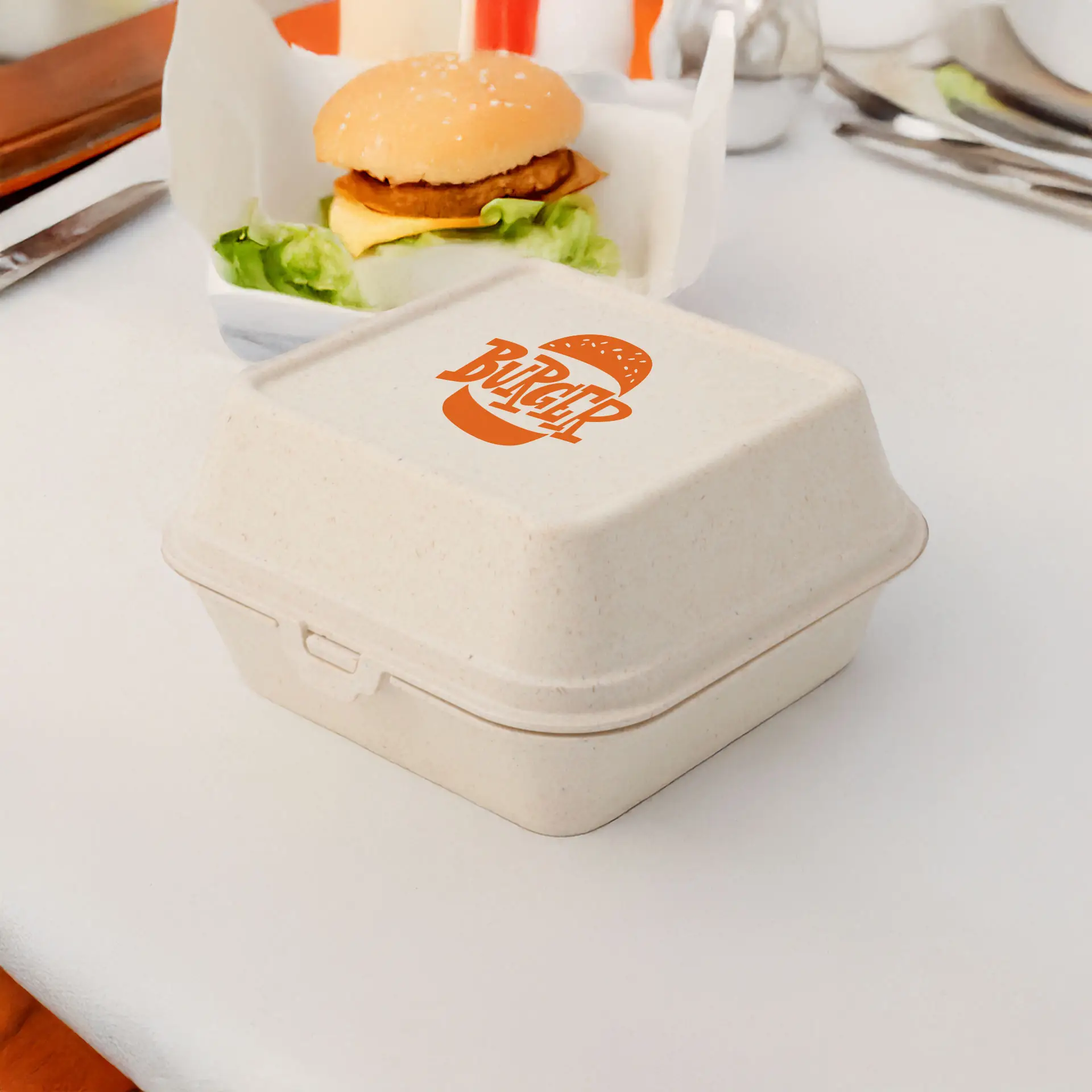 Scatola per hamburger rettangolare bianca crema con logo stampato, posizionata su un tavolo accanto a un hamburger e lattuga.