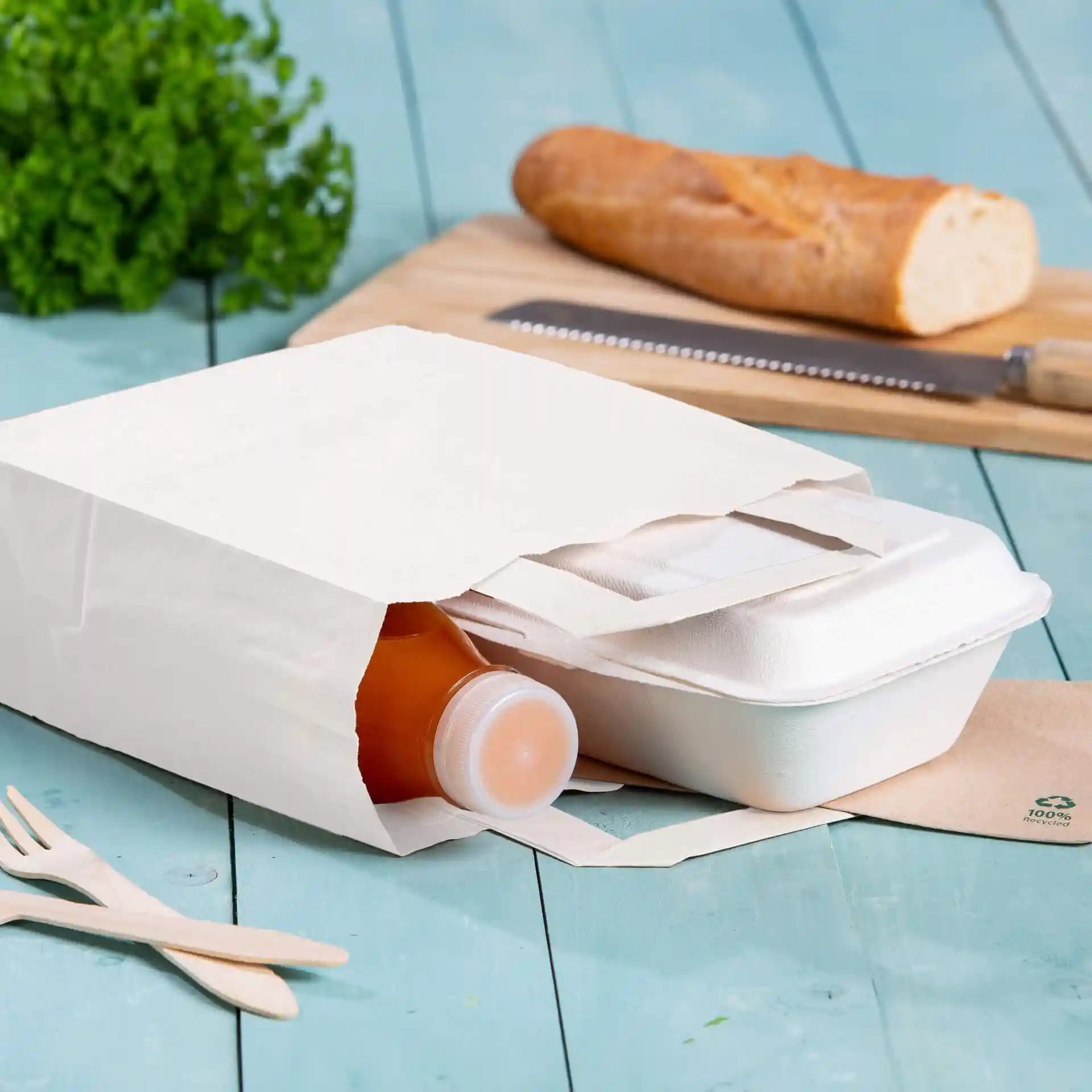 Borsa in carta kraft bianca con una bottiglia e un contenitore da asporto all'interno, posata su una superficie in legno blu.