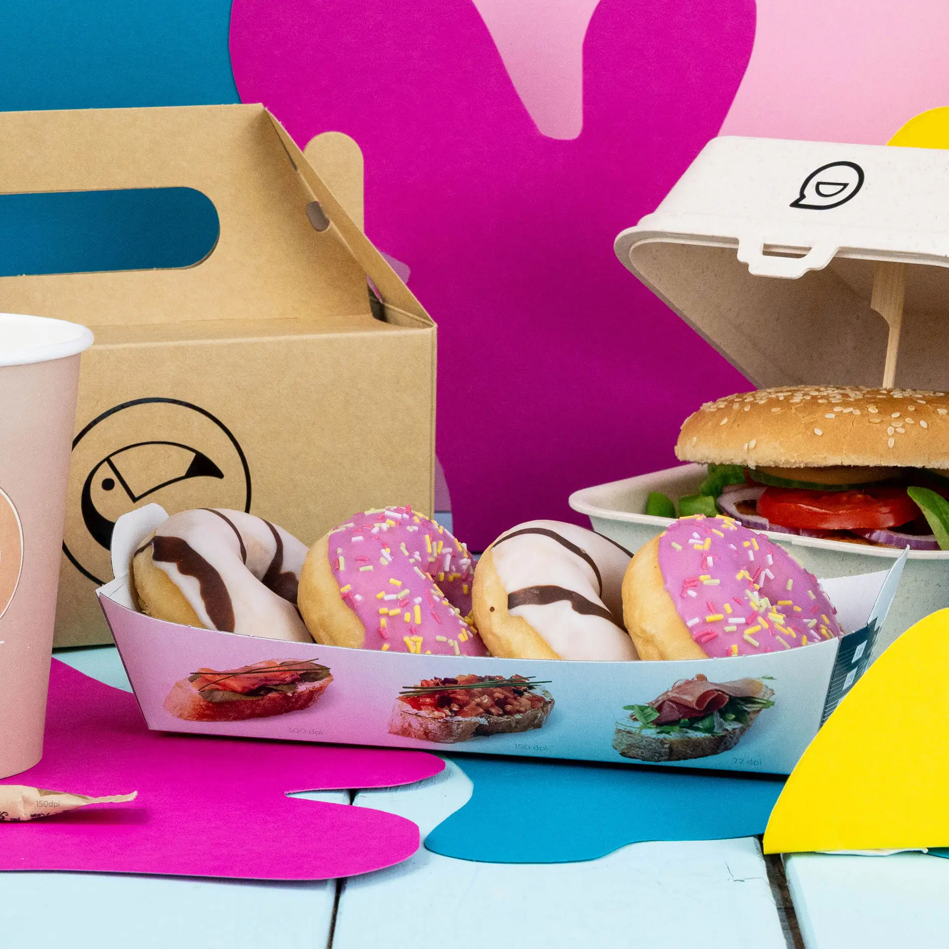 Vassoio rettangolare bianco con quattro ciambelle, un hamburger in un contenitore e una tazza rosa su uno sfondo colorato.