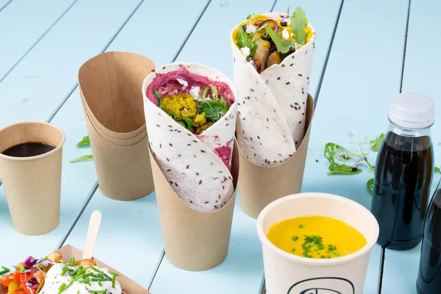 Due alimenti avvolti in bicchieri, uno con ripieno rosa e verdure, l'altro giallo, accanto a una tazza di caffè e zuppa.