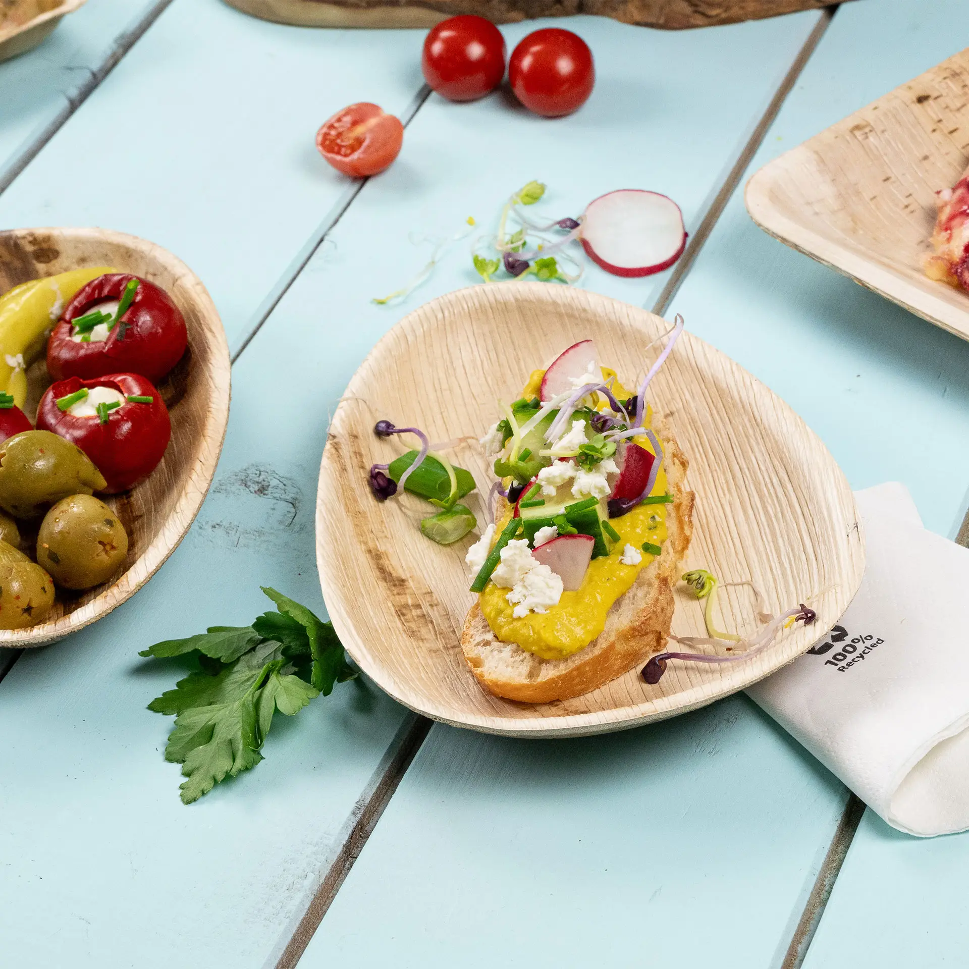 Un piatto a forma di goccia in foglia di palma con un antipasto colorato; olive e pomodori in ciotole vicine.