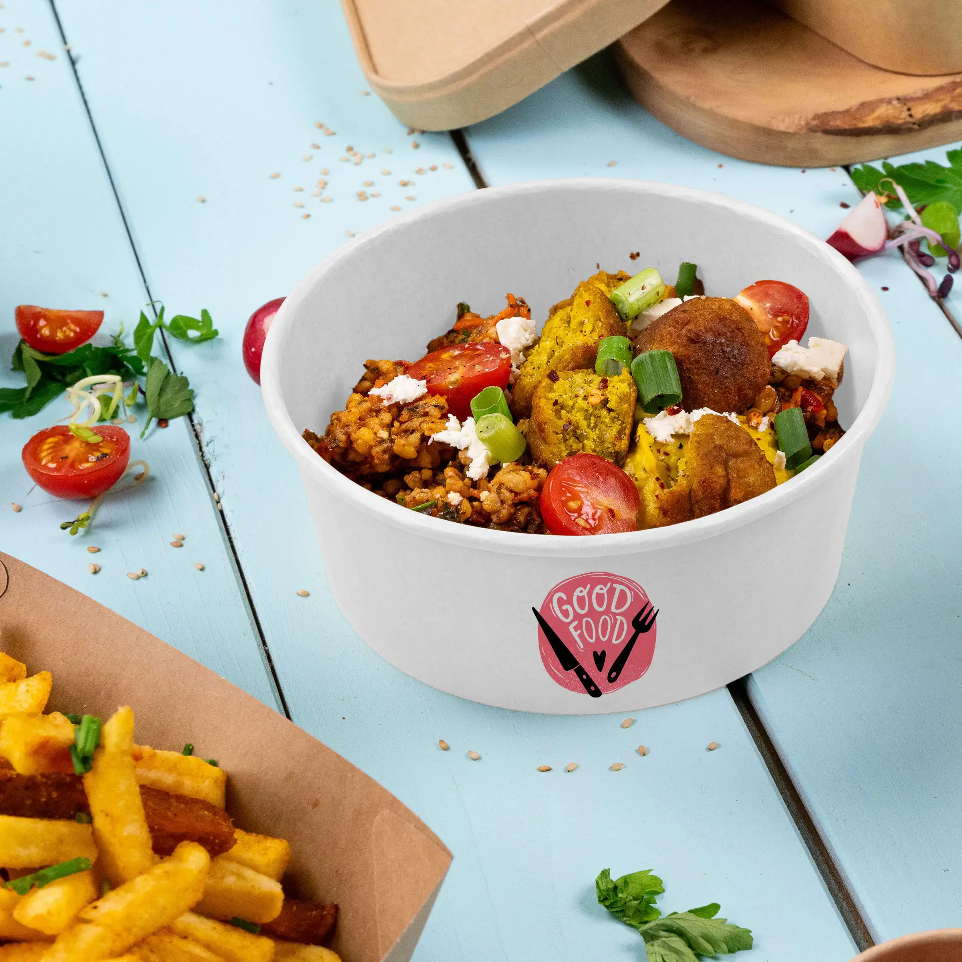 Una ciotola rotonda di cartone bianco riempita con un piatto colorato, con pomodori, cipollotti e falafel, con un logo che dice "CIBO BUONO." Le patatine fritte sono posizionate vicino.