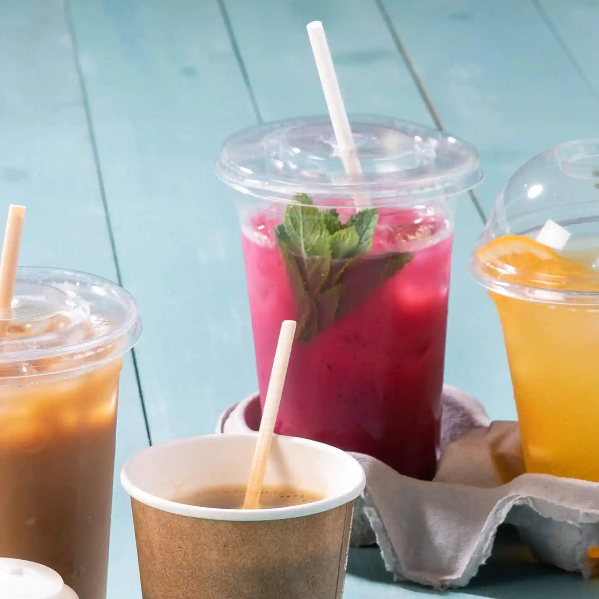 Immagine di diverse bevande in bicchieri trasparenti con cannucce, inclusa una bevanda rosa con foglie di menta e una bevanda marrone in un bicchiere di carta.