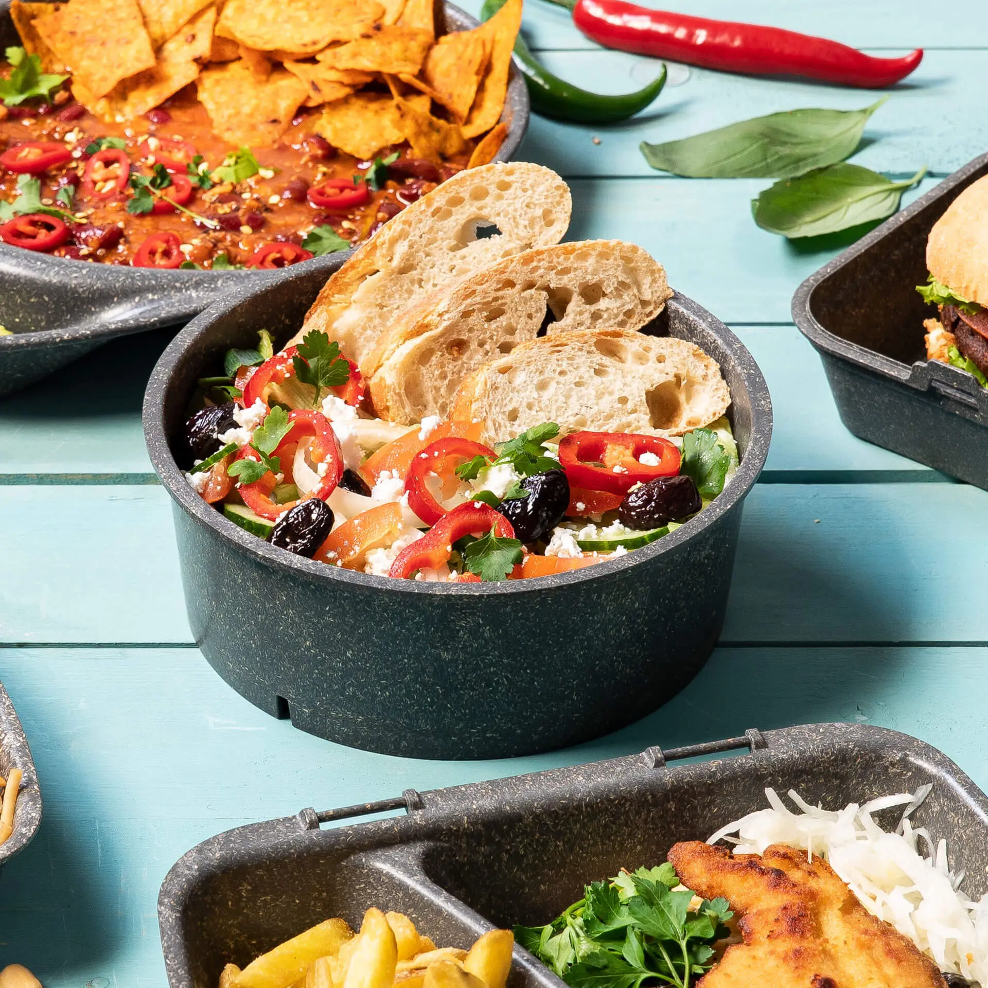 Ciotola Merways riutilizzabile riempita di insalata, guarnita con pomodori a fette, olive ed erbe; servita con fette di pane.