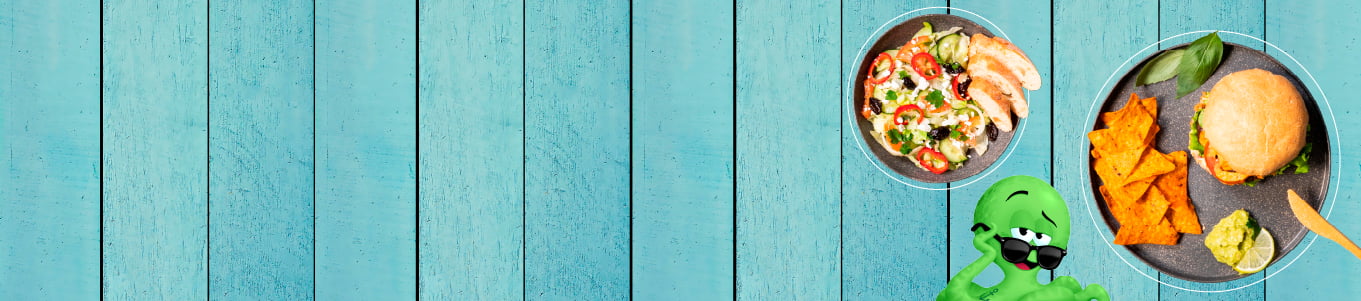 Personaggio cartoon verde accanto a un piatto di nachos, insalata e un panino su uno sfondo in legno blu.