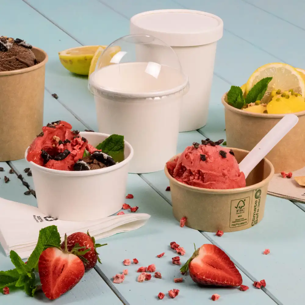 Diverse coppe di gelato con gusti come cioccolato e fragola, guarnite con foglie di menta, su una superficie in legno blu.