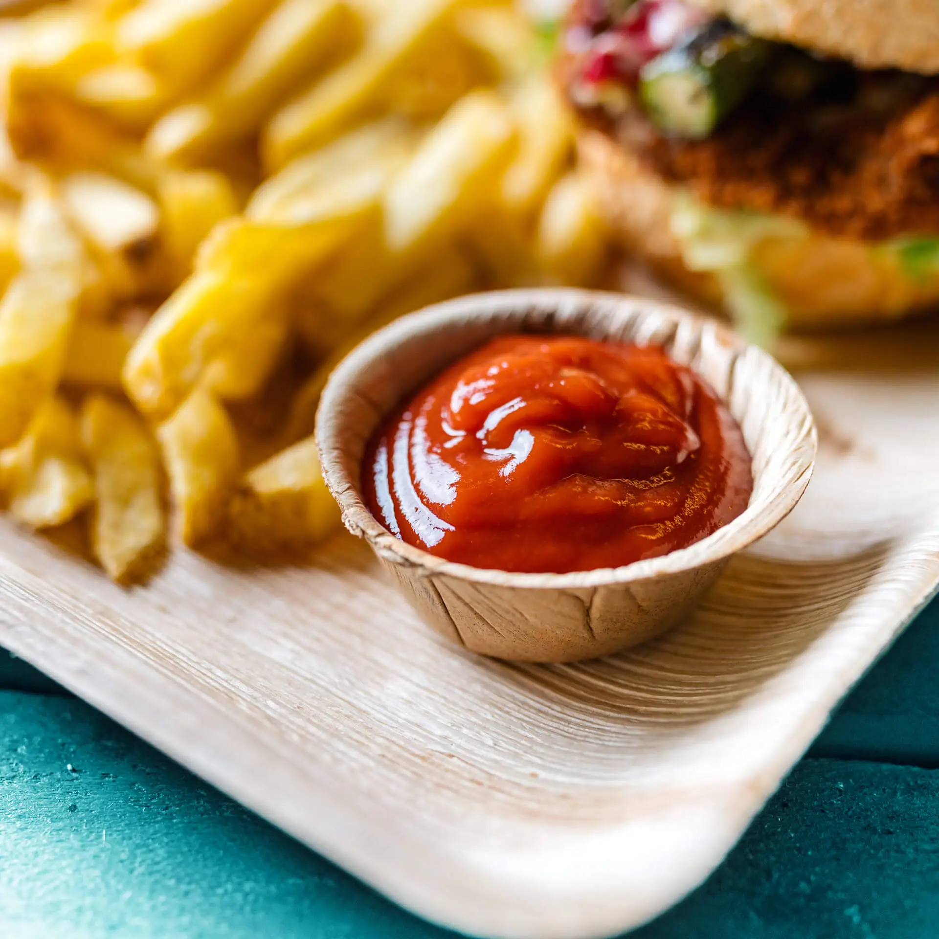 Mini ciotola in foglia di palma contenente ketchup, con patatine sullo sfondo su un vassoio.