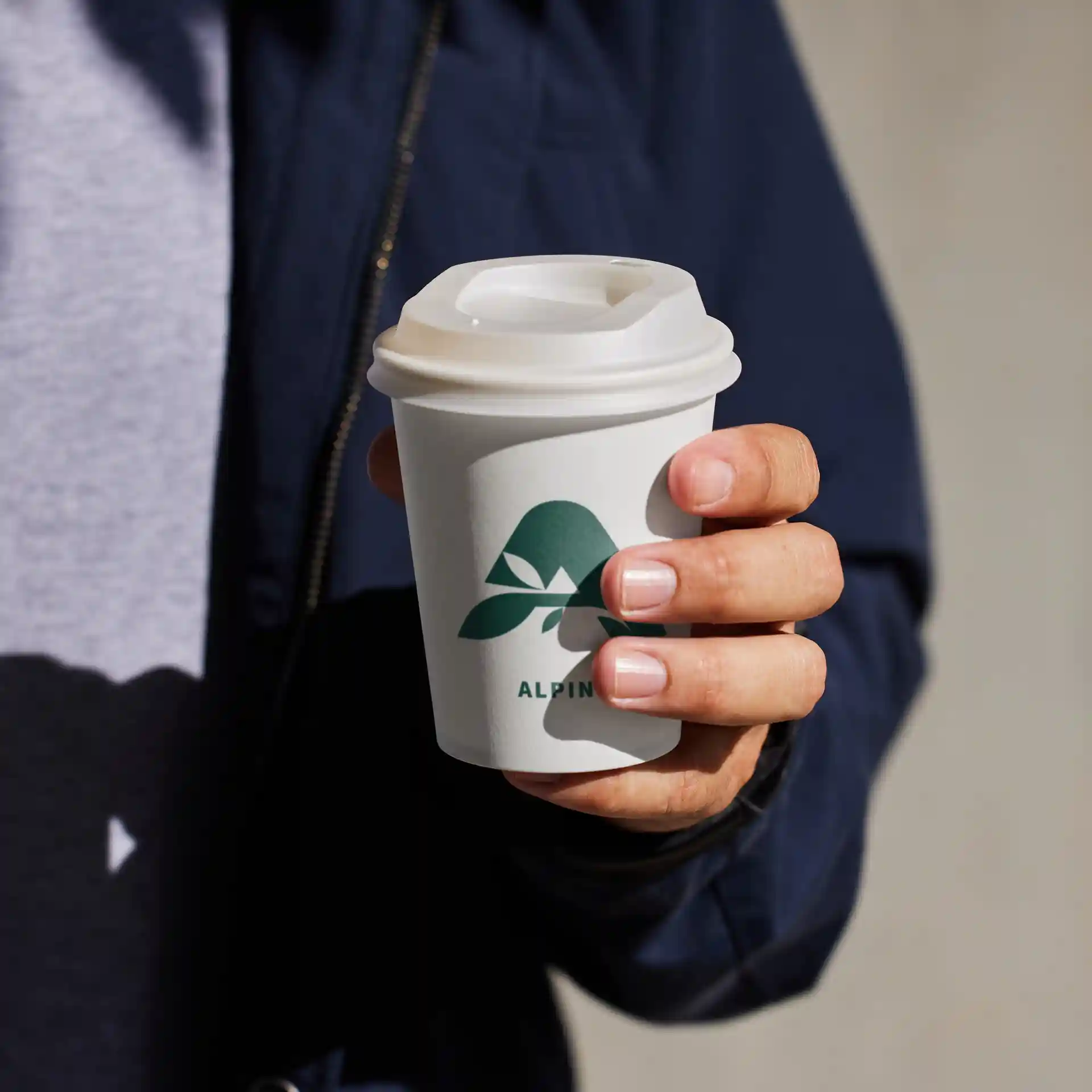 Bicchiere bianco con logo, tenuto in una mano, con coperchio e forma rotonda.