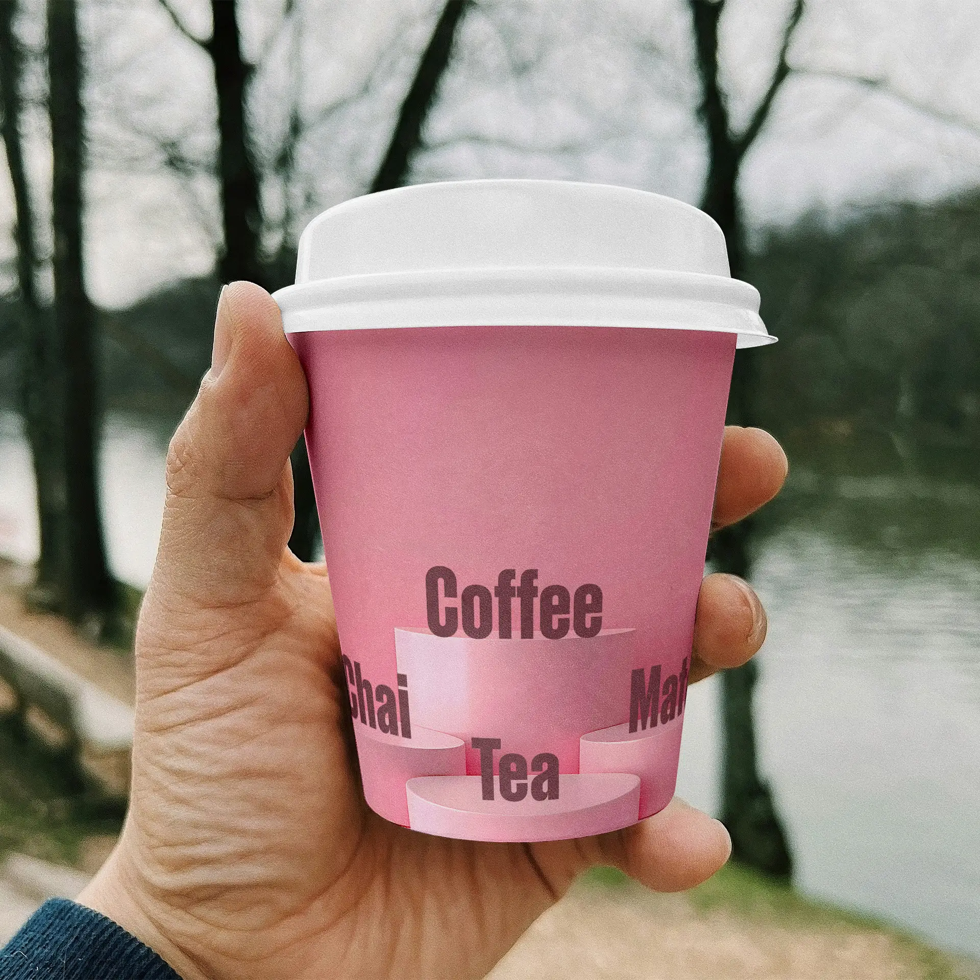 Un bicchiere di carta rosa con le scritte "Caffè", "Chai" e "Tè", tenuto da una mano, con un paesaggio naturale sullo sfondo.