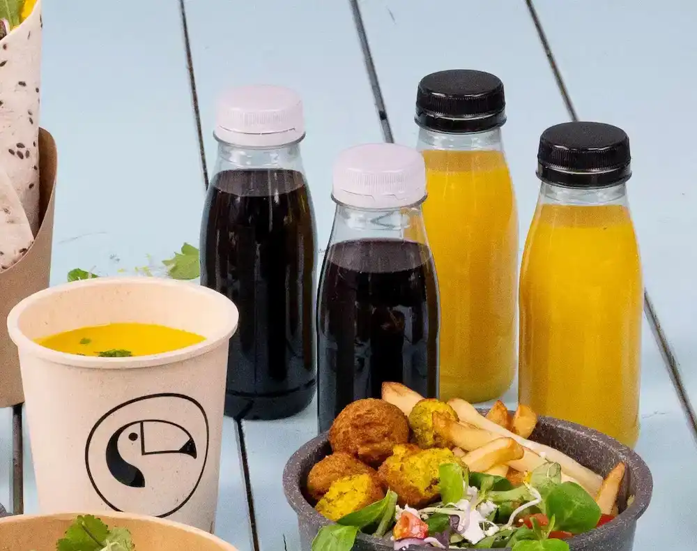Alimenti vari tra cui bottiglie in plastica rPET con varie bevande, una tazza di zuppa e una ciotola di insalata, patatine e falafel.